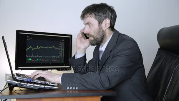 Trader consiglia il cliente su un telefono e guardando il grafico di cambio valuta al computer portatile. Lavori su una borsa cripto — Video Stock