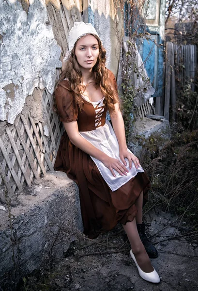 Сумно жінка в сільському плаття сидить біля старих цегляну стіну в старий будинок і намагається білі туфлі плаття. Попелюшка стиль — стокове фото