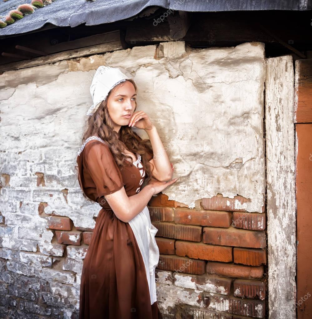 pensive young woman in a rustic dress standing near old brick wall in old house feel lonely. Cinderella style