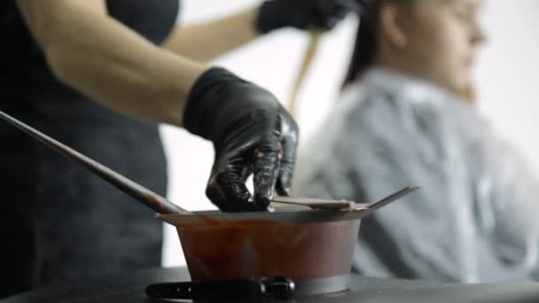 Primer plano cuenco de pintura roja, colorista se agita con un tinte de pincel y el pelo del cliente colorante — Vídeo de stock