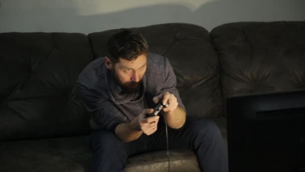 Aantrekkelijke man spelen met een game console op de sofa thuis in donker — Stockvideo