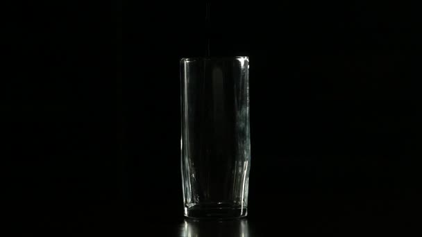 El agua se llena en vidrio sobre un fondo oscuro, cámara lenta — Vídeo de stock