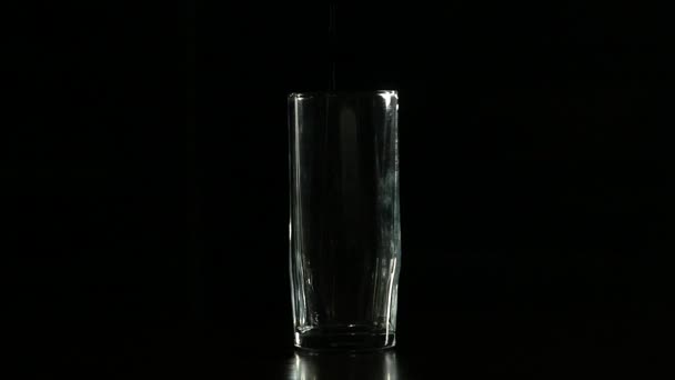 Remplissage d'eau en verre sur un fond sombre, au ralenti — Video