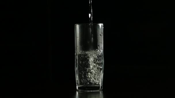 Вода заполняется в стекло на темном фоне, медленное движение — стоковое видео