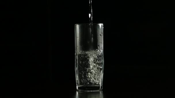 Remplissage d'eau en verre sur un fond sombre, au ralenti 