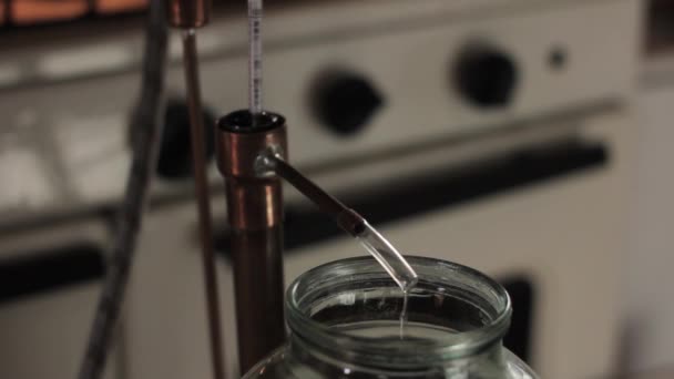Home production of alcohol on flame fire. Alcohol distillation equipment, hooch fluid flow into glass jar — Stock Video
