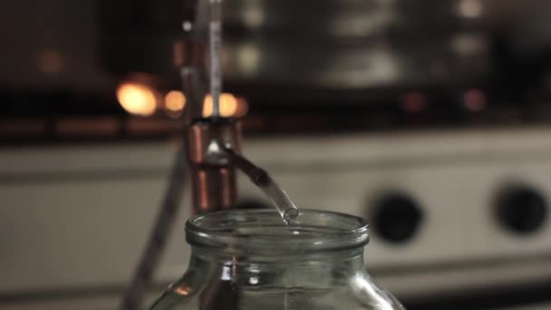Home production of alcohol on flame fire. Alcohol distillation equipment, hooch fluid flow into glass jar — Stock Video