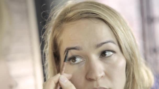 Belle femme blonde qui se maquille tous les jours devant le miroir, dessine les sourcils avec une petite brosse — Video