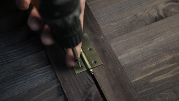 Man is fastening the door hinge to the furniture detail using electric drill — Stock Video