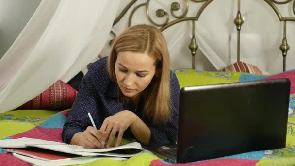 Όμορφη γυναίκα που σπουδάζουν σε ένα κρεβάτι στο δωμάτιό της με το laptop. on-line εκπαίδευση — Αρχείο Βίντεο