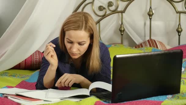 Mooie vrouw online onderwijs in huis. Student op een bed met werkmap en laptop. Slow motion — Stockvideo