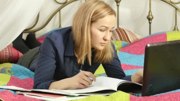 Hermosa mujer en línea la educación en el hogar. Estudiante en una cama con cuaderno de trabajo y portátil. 4K — Vídeos de Stock