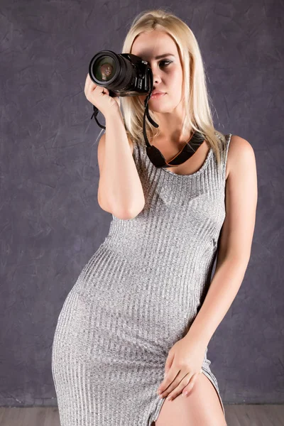 Jeune femme blonde en robe grise tenant caméra. Photographe faisant des photos . — Photo