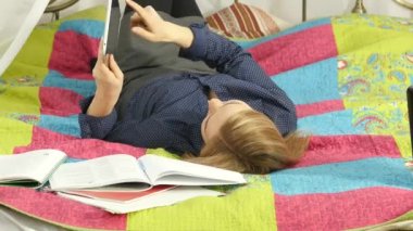 Yatakta yatan dijital tablet okuma dostça kız öğrenci. güzel bir kadın evinde on-line eğitim. 4k