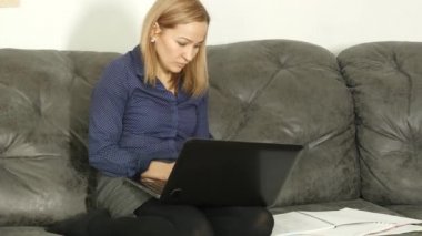 Çalışma kitabı ve bir dizüstü bilgisayar ile bir divan okuyan bir kadın. on-line eğitim içinde ev. 4k