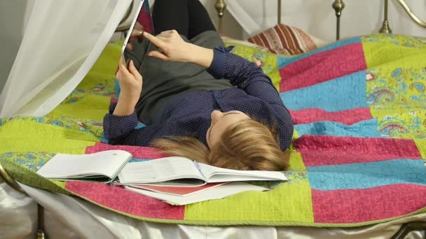 Freundliche Studentin liest auf digitalem Tablet im Bett liegend. schöne Frau Online-Bildung zu Hause. Zeitlupe — Stockvideo