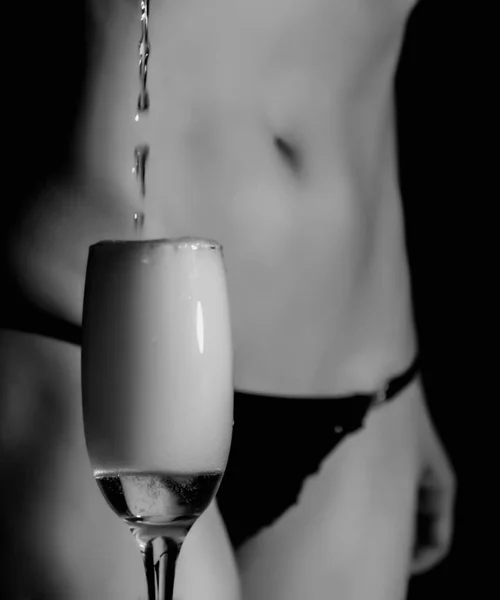 Sexy cuerpo mujer en negro ropa interior vierte champán en vidrio. blanco y negro —  Fotos de Stock