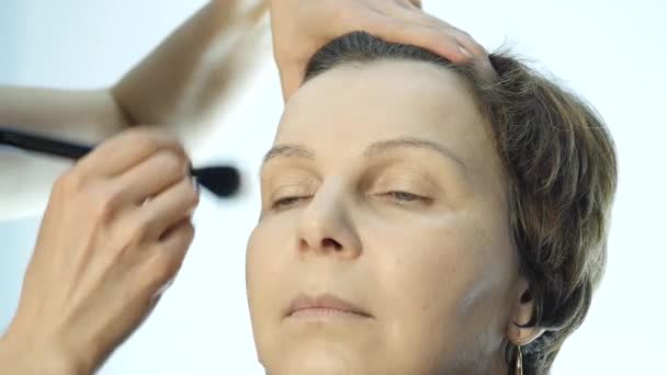 Primer plano del maquillador profesional que hace el maquillaje diario, pone polvo en las mejillas de las mujeres con cepillo — Vídeos de Stock