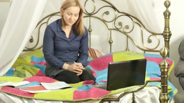 On-line εκπαίδευση στο σπίτι με το βιβλίο εργασίας και φορητού υπολογιστή. όμορφη γυναίκα χρησιμοποιεί το smartphone για βίντεο chat με τους συμμαθητές. 4k — Αρχείο Βίντεο