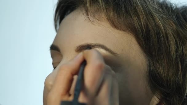 Close-up de maquilhador profissional aplicando delineador na pálpebra. Stylist está fazendo maquiagem para a fêmea por eyeliner — Vídeo de Stock