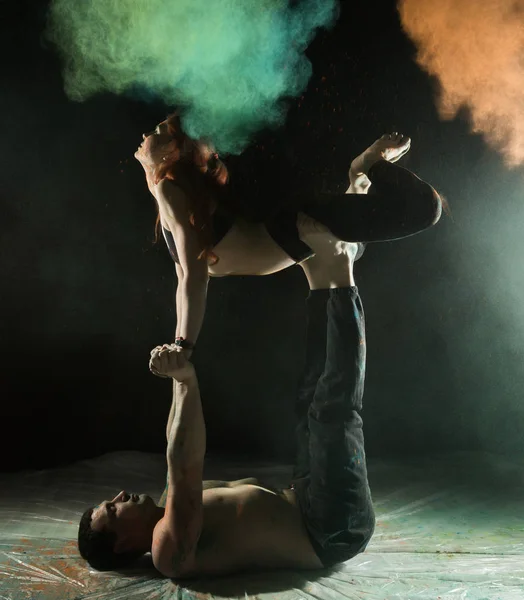 Mladý sportovní pár dělá acroyoga cvičení v temné místnosti s barevný kouř — Stock fotografie