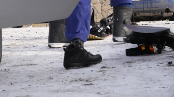 Homem coloca sapatos para snowboard perto do carro em um estacionamento de montanha — Vídeo de Stock