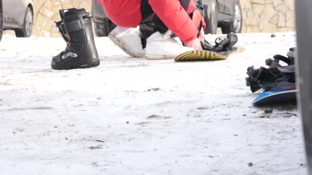 Man puts on shoes for snowboarding near the car on a mountain parking — Stock Video