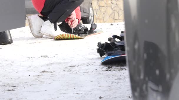 Člověk klade na boty pro snowboarding poblíž auto na horu parkování — Stock video