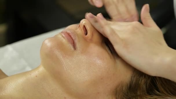 Schöne Frau bekommt Gesichtsmassage im Wellnessbereich. Gesichtspflege im Schönheitssalon. Zeitlupe — Stockvideo