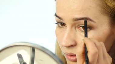 Güzel kadın kaşları ve günlük makyaj makyaj fırçası küçük ayna önünde ile boyar. 4k