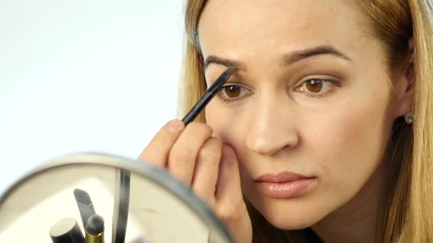 Hermosa mujer pinta sus cejas y hacer maquillaje diario con cepillo de maquillaje delante de un pequeño espejo. cámara lenta — Vídeos de Stock