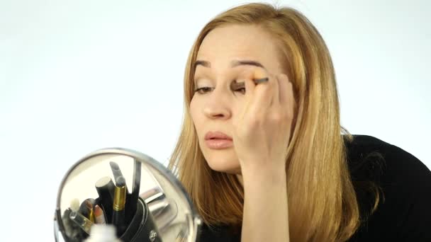 Mujer rubia se pinta las pestañas y hace maquillaje diario con pincel delante de un pequeño espejo. cámara lenta — Vídeos de Stock
