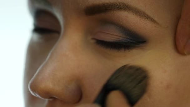 Primer plano del maquillador profesional que hace el maquillaje diario, pone polvo en las mejillas de las mujeres con cepillo — Vídeo de stock