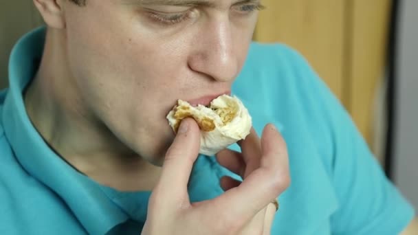Smal man äter snabbmat mellanmål med stor njutning. killen tuggar skräpmat med stor aptit. slowmotion — Stockvideo