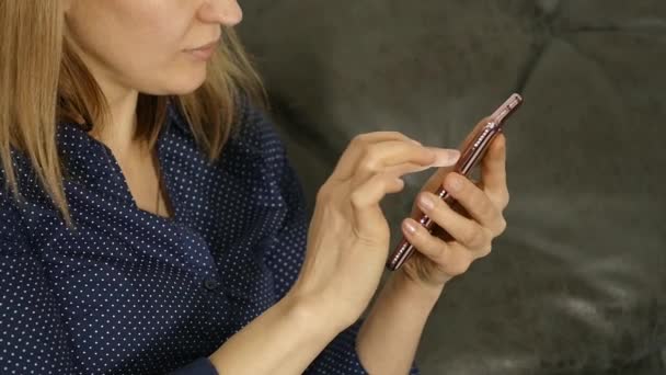 Mujer rubia en casa sentada en un sofá y usando un smartphone — Vídeo de stock