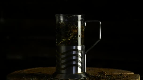 Öntsük a forró vízzel levelek egy üveg teáskanna tea egy sötét háttér. lassú mozgás — Stock videók