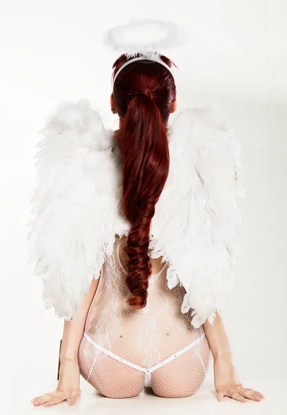 Sexy roodharige vrouw in Angel pak op een lichte achtergrond. Achteraanzicht van een gevallen engel. — Stockfoto