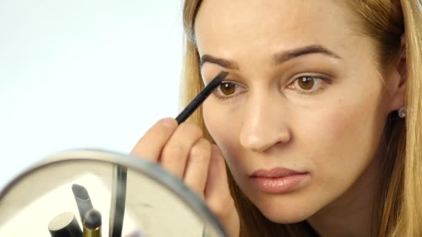 Vacker kvinna målar ögonbrynen och gör dagliga makeup med makeup borste framför liten spegel. slowmotion — Stockvideo