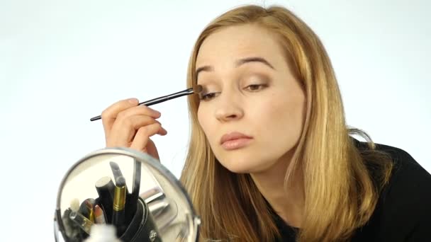 Hermosa mujer pinta sus cejas y hacer maquillaje diario con cepillo de maquillaje delante de un pequeño espejo. cámara lenta — Vídeos de Stock