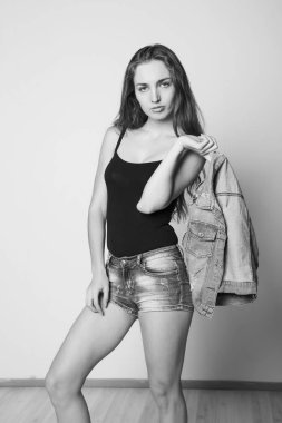 genç güzel mutlu şık hippi kız bir kot ceket ve hafif bir arka plan üzerinde poz şort. siyah ve beyaz