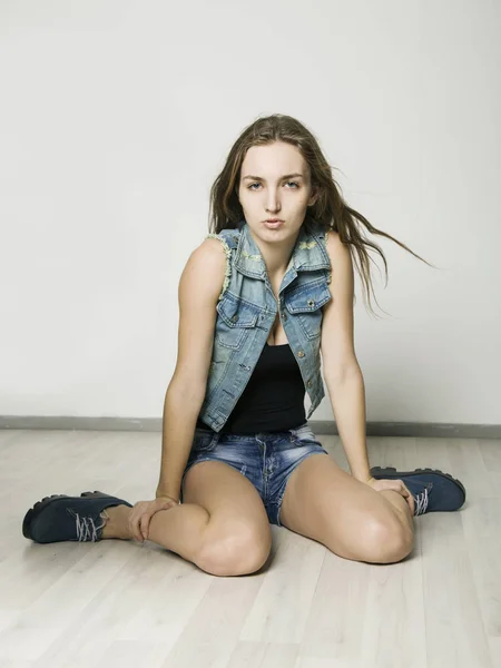 Alegre sorridente hipster menina em uma jaqueta de ganga e shorts posando em um fundo leve — Fotografia de Stock