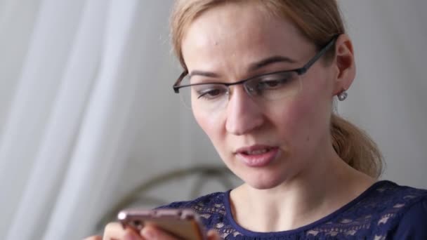 Mujer de negocios rubia en gafas comprobando algo en el teléfono inteligente. 4K — Vídeo de stock