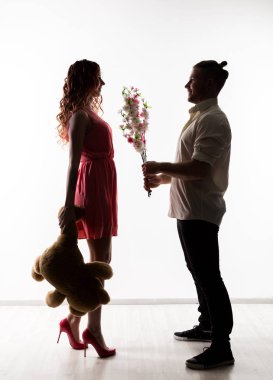 Kız bir tarih bir adamla. çiçekler ve oyuncak ayı tutan kadın tutan adam. hafif bir arka plan üzerinde siluet