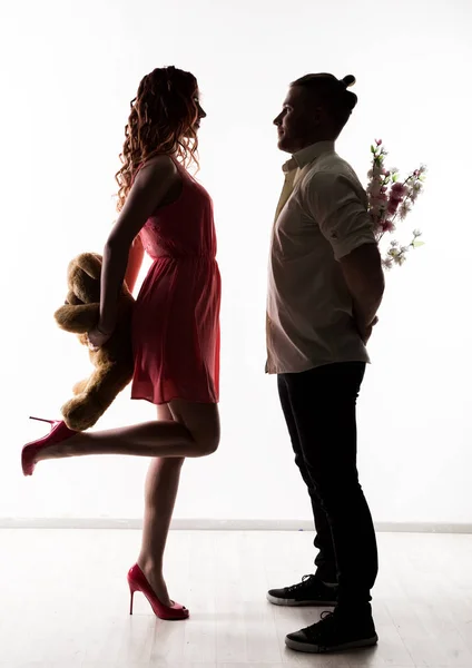 日男と少女。花とクマのぬいぐるみを持った女性を抱きかかえた。明るい背景にシルエット — ストック写真