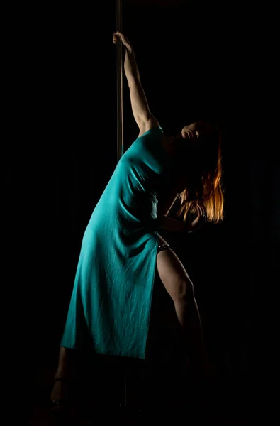 Sexig kvinna pole dansare i en lång turkos klänning med en skåra på en mörk bakgrund — Stockfoto
