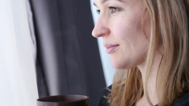 Молода жінка п'є каву або чай біля вікна. 4-кілометровий — стокове відео