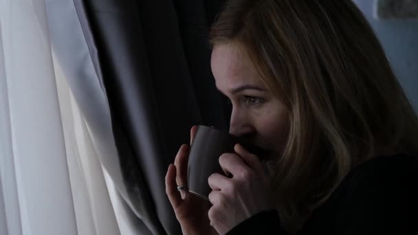 Beautiful woman drinks coffee or tea looking out the window. slow motion — Stock Video