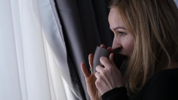 Mulher bonita bebe café ou chá olhando pela janela. câmara lenta — Vídeo de Stock
