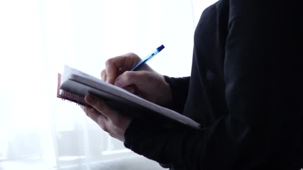 Jovem estudante escreve em seu diário de pé perto da janela. experiências de adolescentes. 4K — Vídeo de Stock