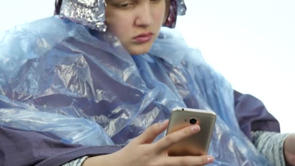 Chica hablando por teléfono mientras que la peluquería hace peinado, tinte para un adolescente en un salón de belleza. 4K — Vídeos de Stock